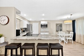 A modern kitchen with a central island, white cabinetry, and a microwave. There are three stools at the island and a dining table with chairs.