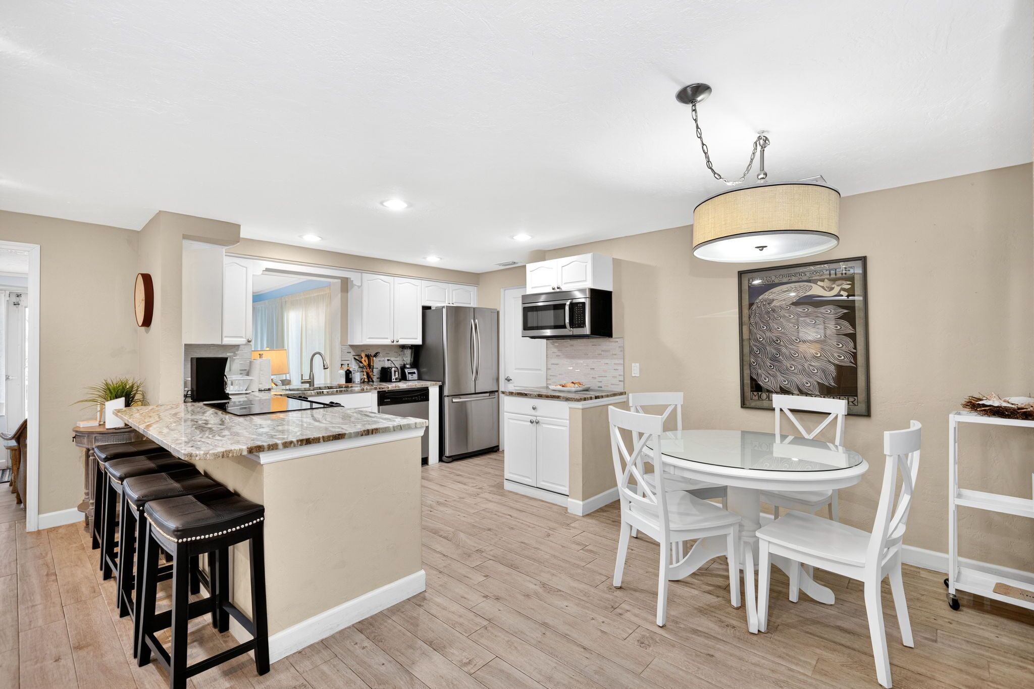 A modern kitchen with a central island, stainless steel appliances, and a dining area with white chairs.