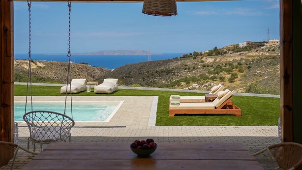 A wooden deck with a swing chair, a pool, and lounge chairs with cushions. - Oliva Emerald Eco - Secluded Off-grid Vineyard Villa (Hersonissos)