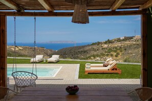 Eine Holzterrasse mit Schaukelstuhl, Pool und Liegestühlen mit Kissen.