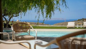 A poolside area with lounge chairs and a table, overlooking a clear blue sea and distant mountains. - Oliva Emerald Eco - Secluded Off-grid Vineyard Villa (Hersonissos)