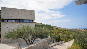 A modern building with stone walls and a pathway lined with trees. - Oliva Emerald Eco - Secluded Off-grid Vineyard Villa (Hersonissos)