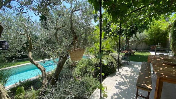 A poolside area with a wooden table and chairs, surrounded by lush greenery and trees. - Charming Villa With AC in Alpilles (Paradou)
