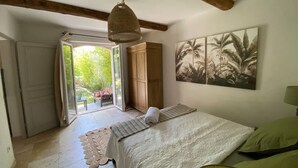 A bedroom with a bed, a wardrobe, a door leading to a balcony, and a wall with a tropical plant painting. - Charming Villa With AC in Alpilles (Paradou)