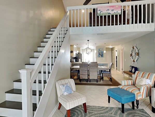 A spacious living area with a staircase, a dining area, and a view of the kitchen.