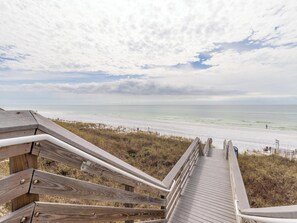 A wooden boardwalk leading to a beach with a view of the ocean and sky.