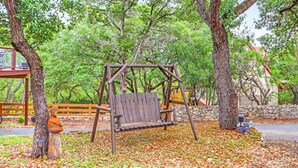 Un ensemble de balançoires en bois dans un parc, avec des arbres et un mur de pierre en arrière-plan.