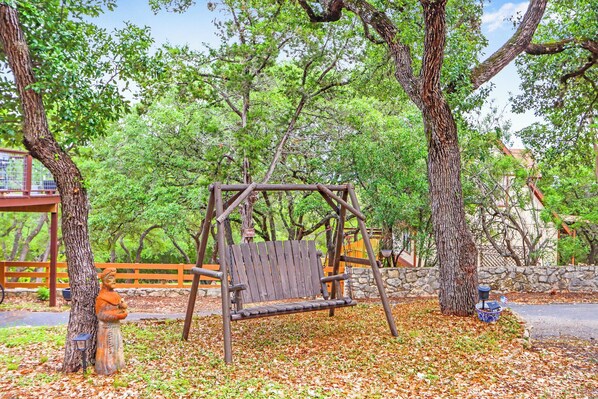 Un ensemble de balançoires en bois dans un parc, avec des arbres et un mur de pierre en arrière-plan.