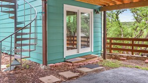 Une maison turquoise avec un escalier en colimaçon, une terrasse en bois et un chemin de pierre menant à une porte.