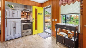 Une cuisine avec des murs en bois, une porte jaune, des appareils électroménagers en acier inoxydable et une vue sur l’extérieur.