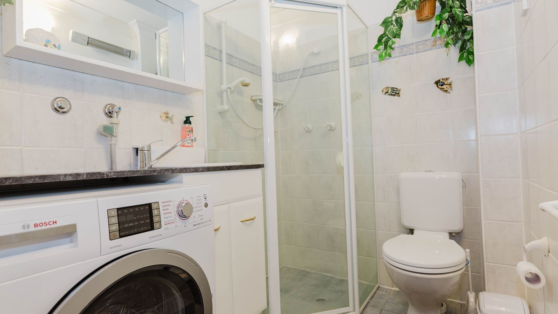 A modern bathroom with a Bosch washing machine, a glass-enclosed shower, and a toilet.