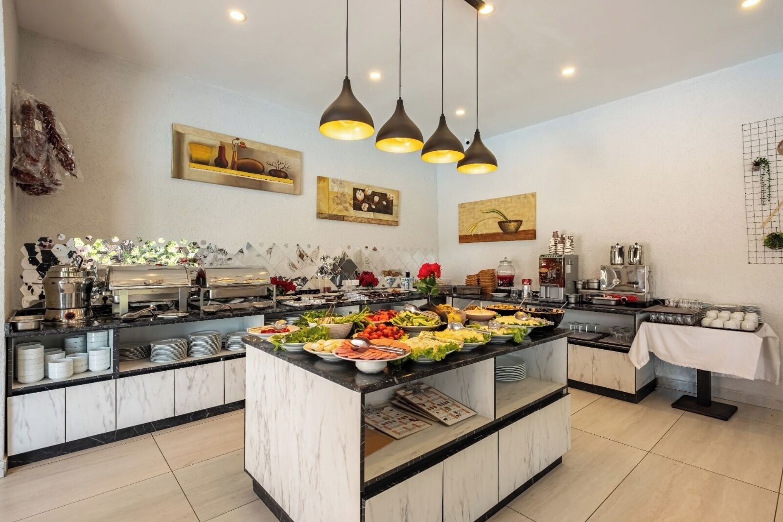 A modern kitchen with a marble countertop, buffet setup, and hanging pendant lights.