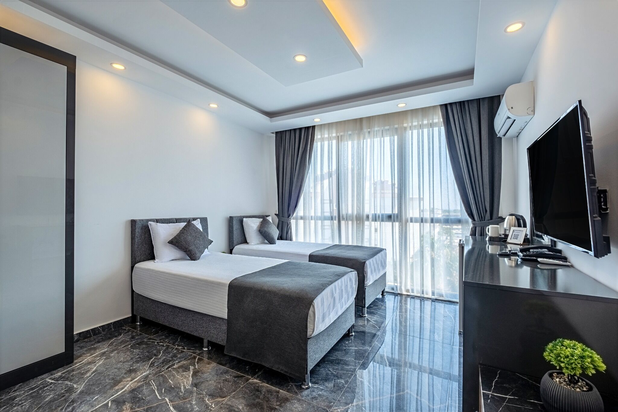 Une chambre d’hôtel moderne avec deux lits, un bureau doté d’un téléviseur à écran plat et une grande fenêtre avec des rideaux.