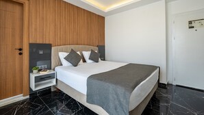 Ένα σύγχρονο δωμάτιο ξενοδοχείου με κρεβάτι, ξύλινο επενδυμένο τοίχο, λευκούς τοίχους και μαρμάρινο δάπεδο.