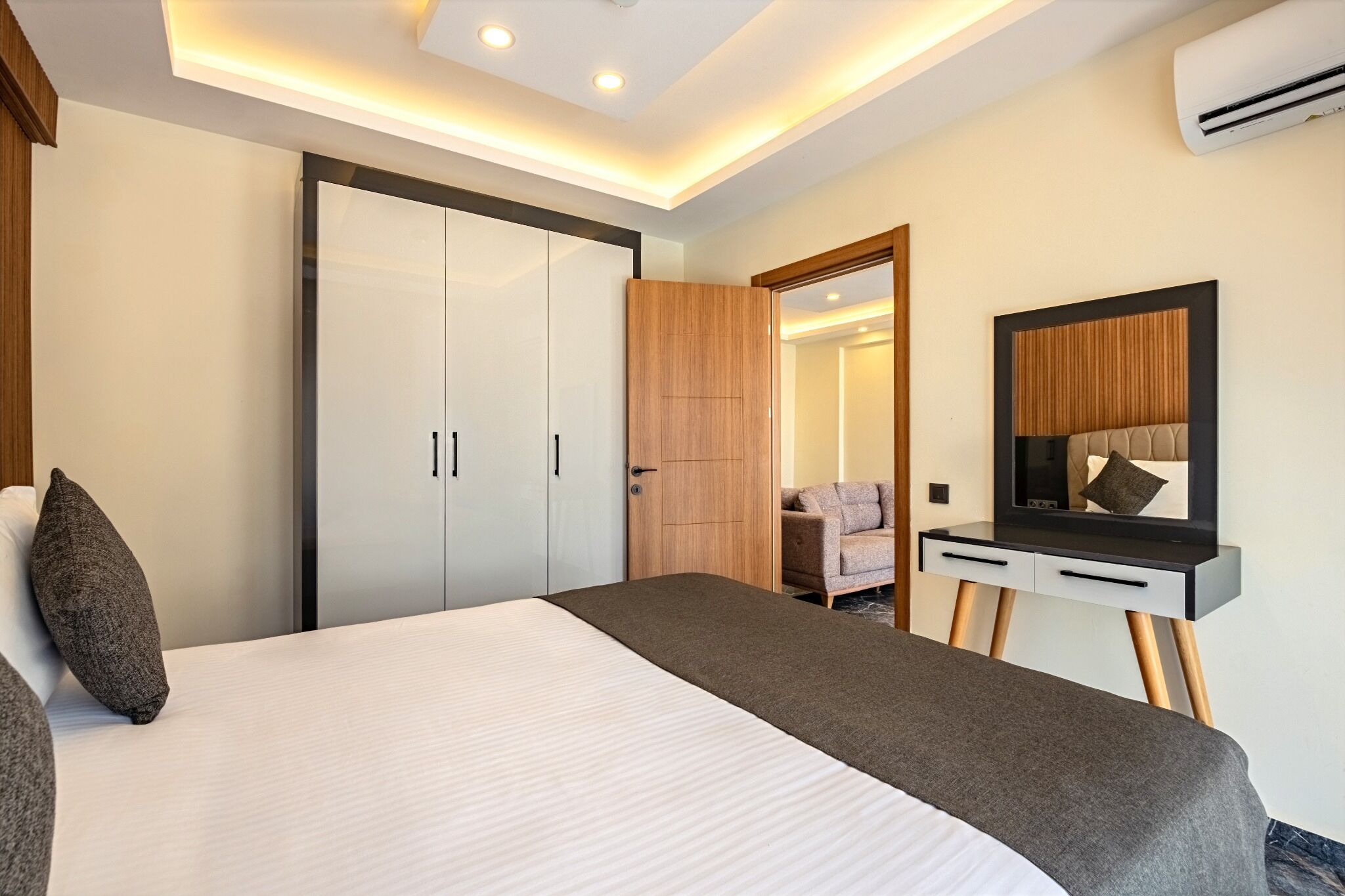Una habitación de hotel moderna con una cama grande, un armario, un escritorio con espejo y una zona de estar.