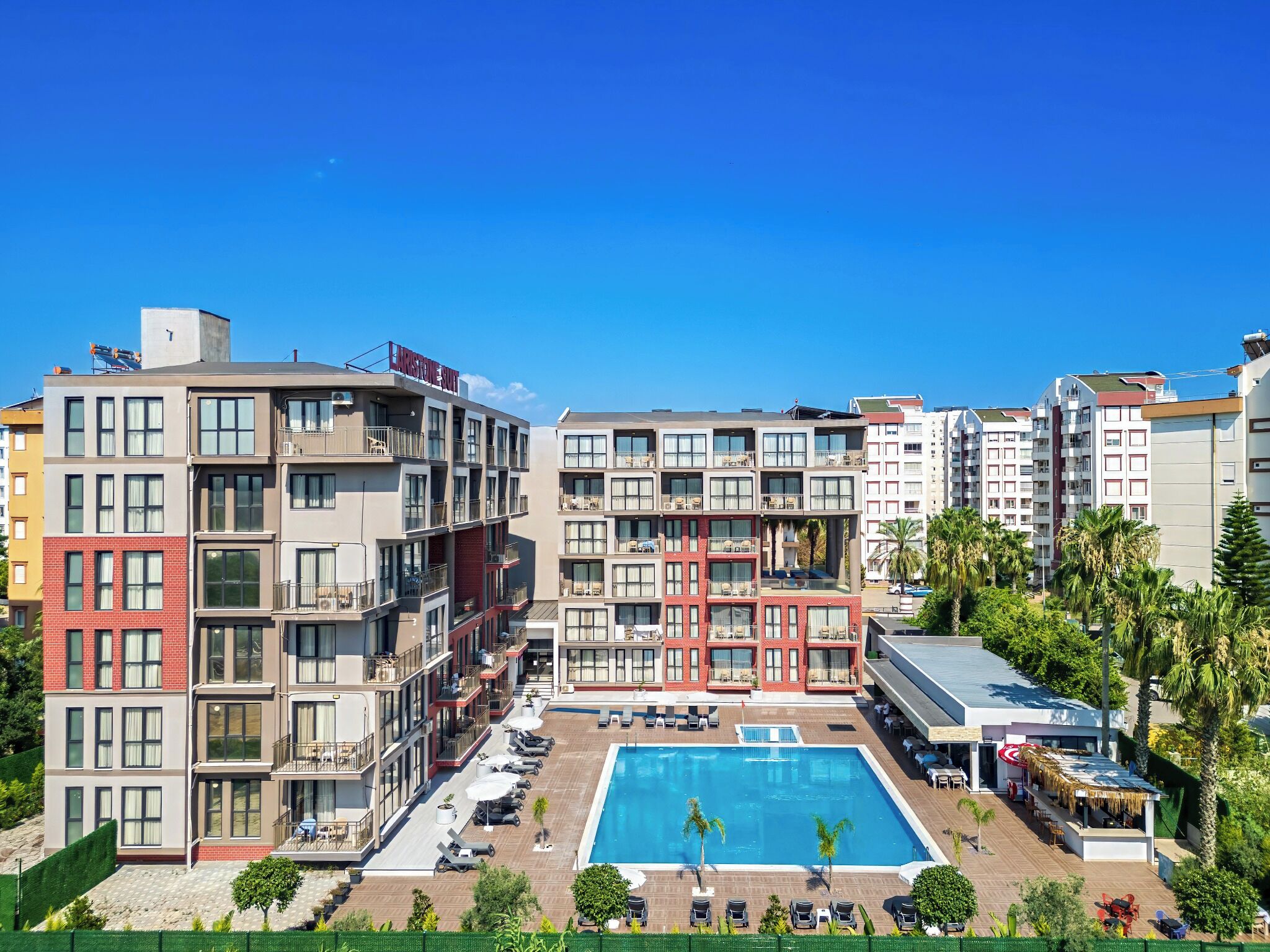 Um hotel com vários andares, piscina no terraço, varandas e um céu azul límpido.