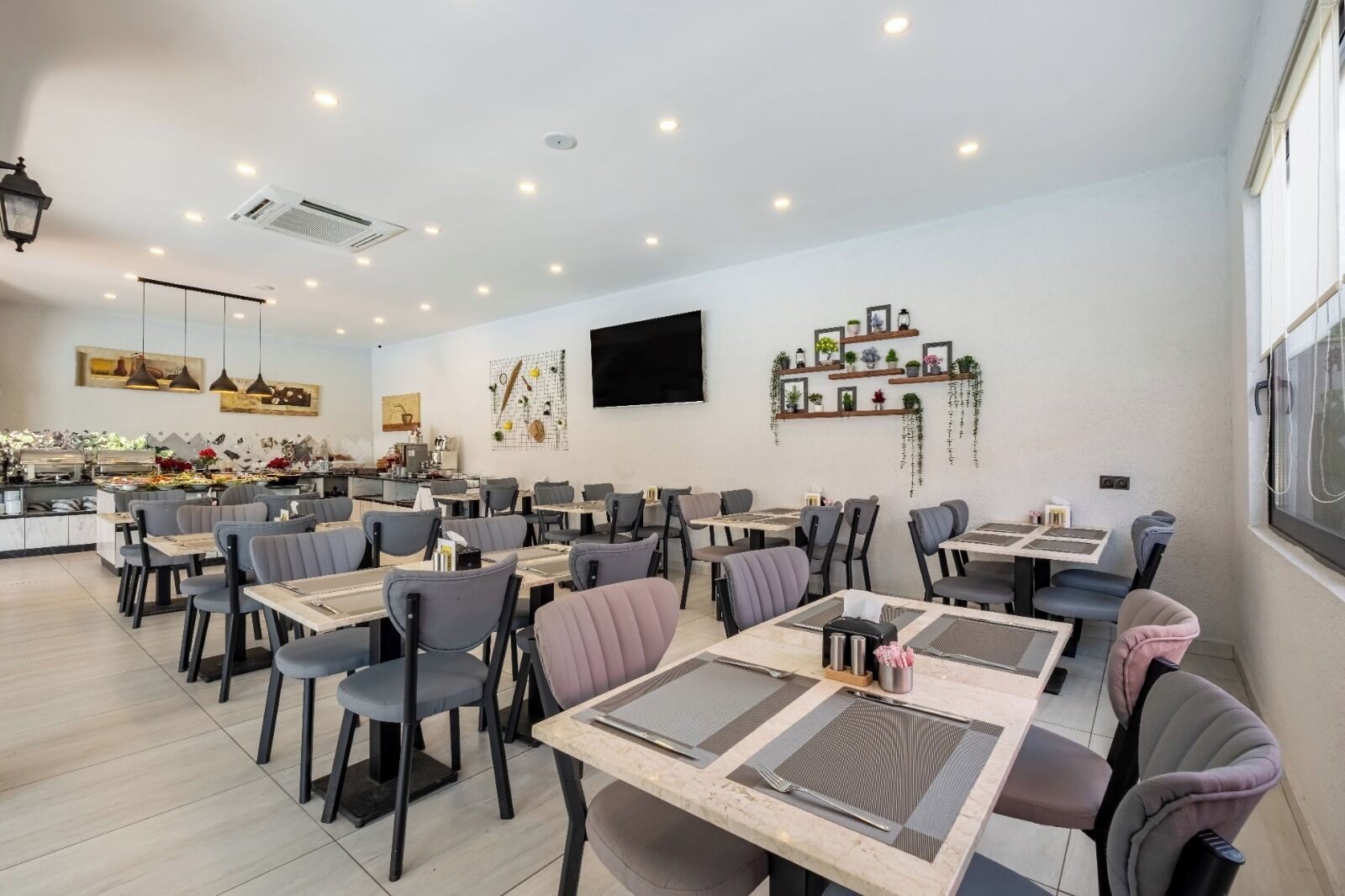 A modern dining area with multiple tables and chairs, a kitchen in the background, and decorative wall art.