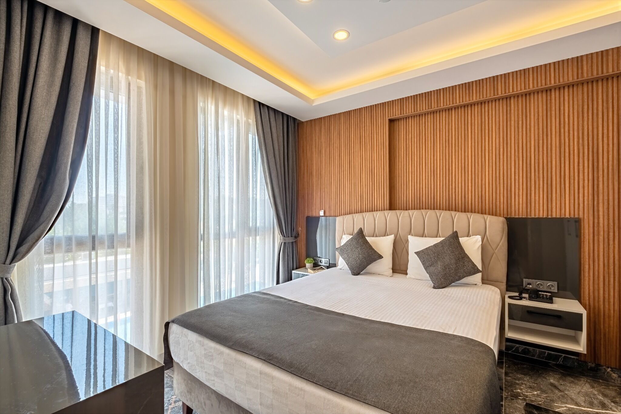 A modern hotel room with a large bed, a bedside table, a TV, and a view of the outdoors.