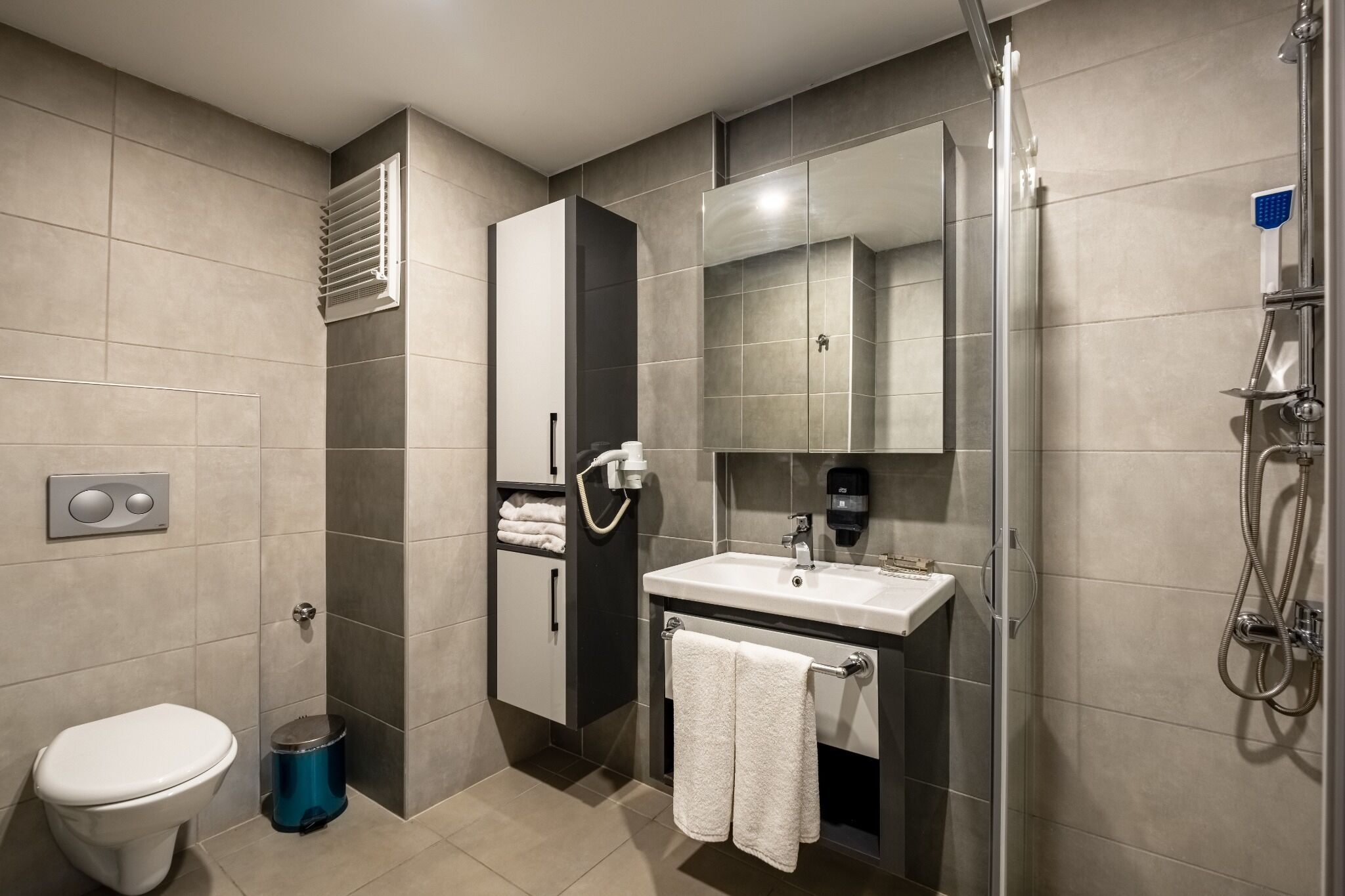 A modern bathroom with a toilet, sink, mirror, shower, and towel rack.