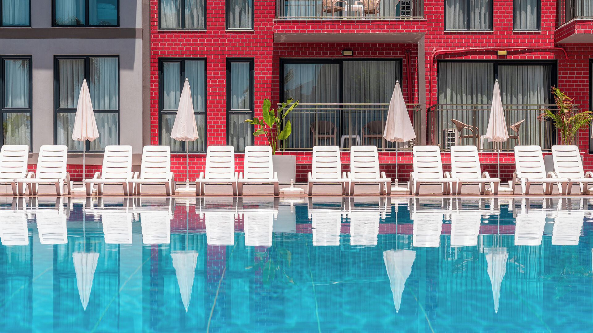A poolside area with white lounge chairs and umbrellas, a red brick building, and a clear blue pool.