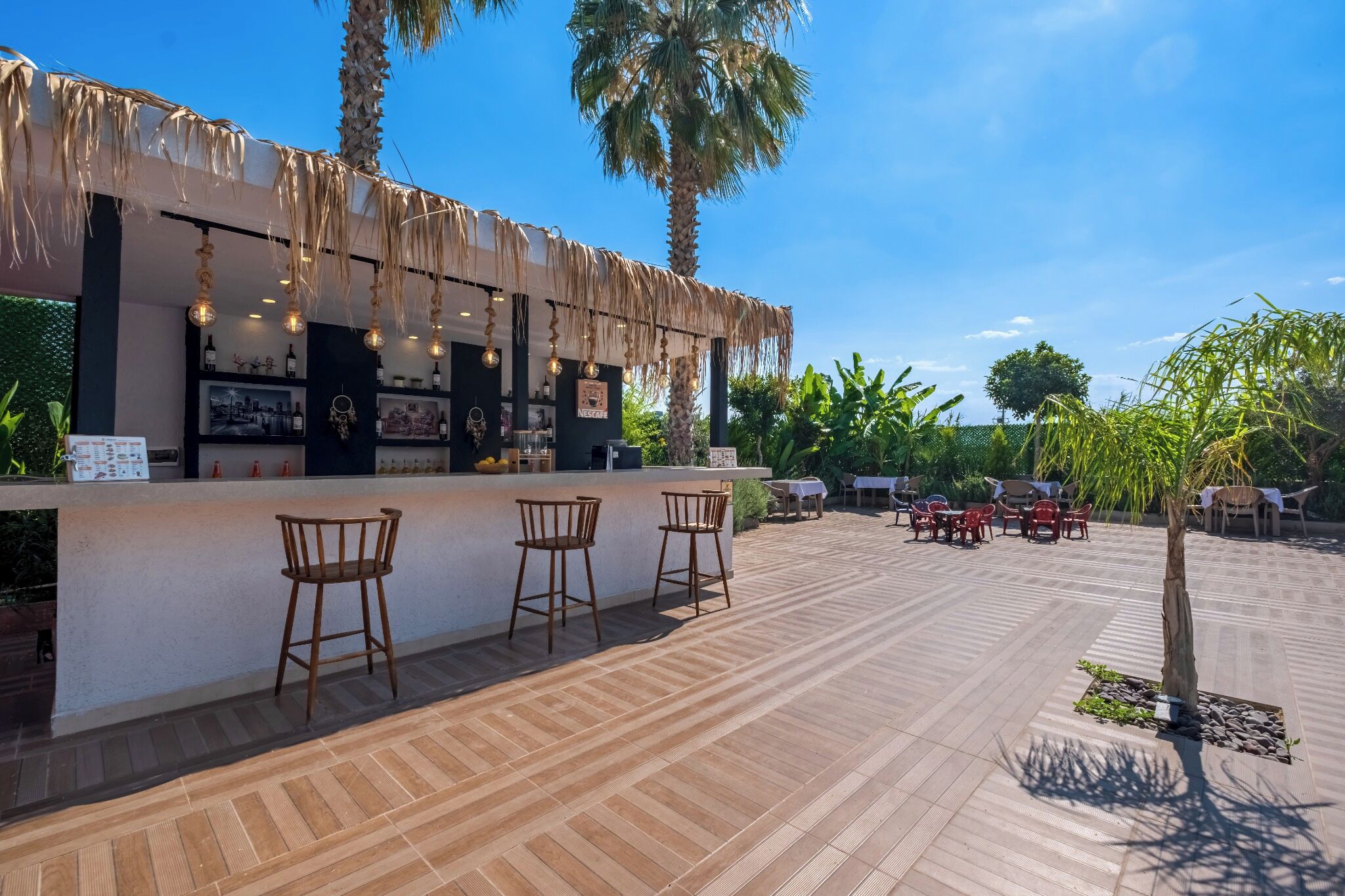Un área de bar al aire libre con sillas de madera, una barra con menú y palmeras al fondo.