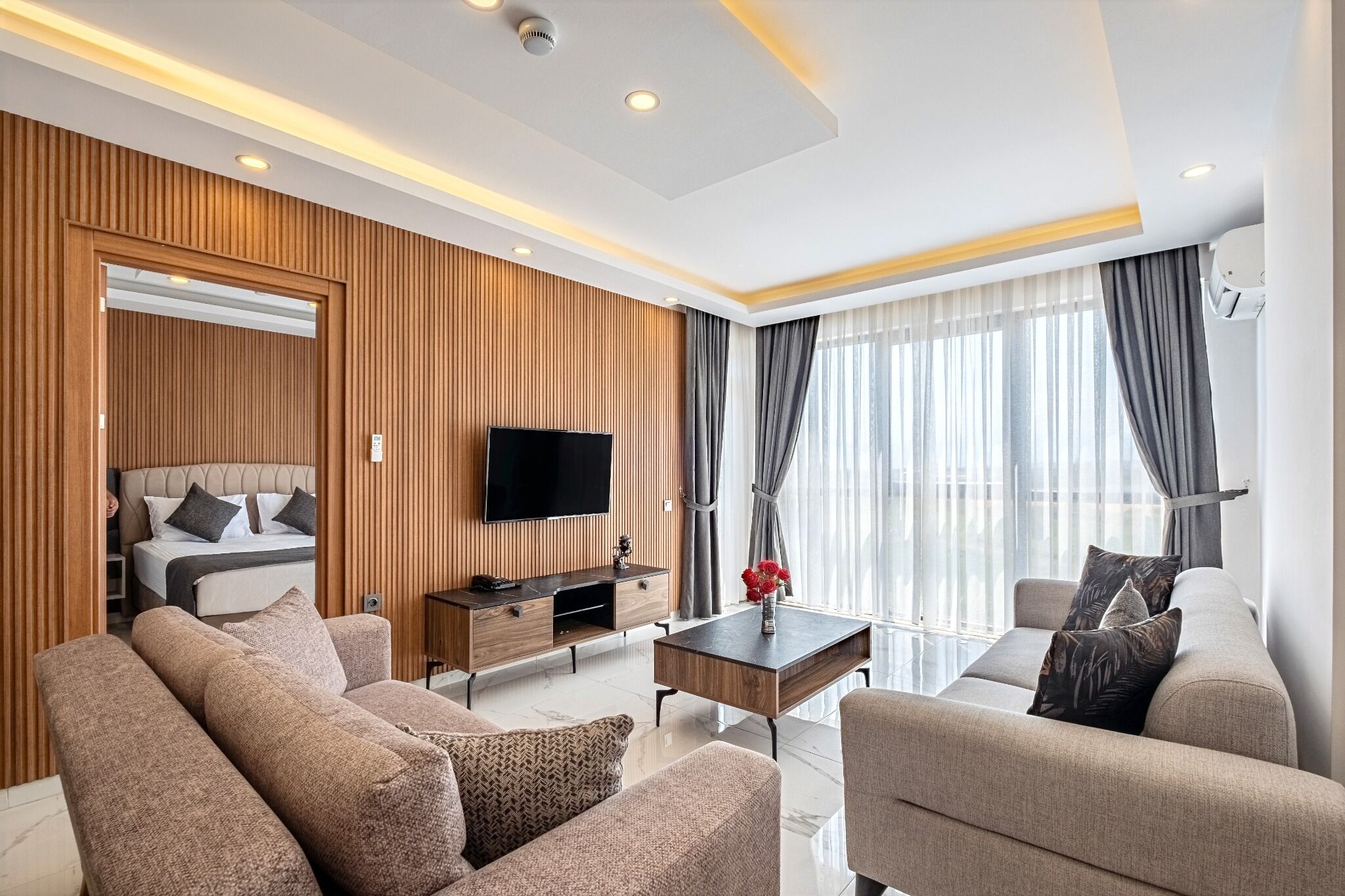 Habitación de hotel moderna con cama, sofá, televisión y zona de comedor.