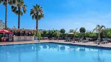 Piscina com espreguiçadeiras e área de bar com um guarda-sol vermelho.