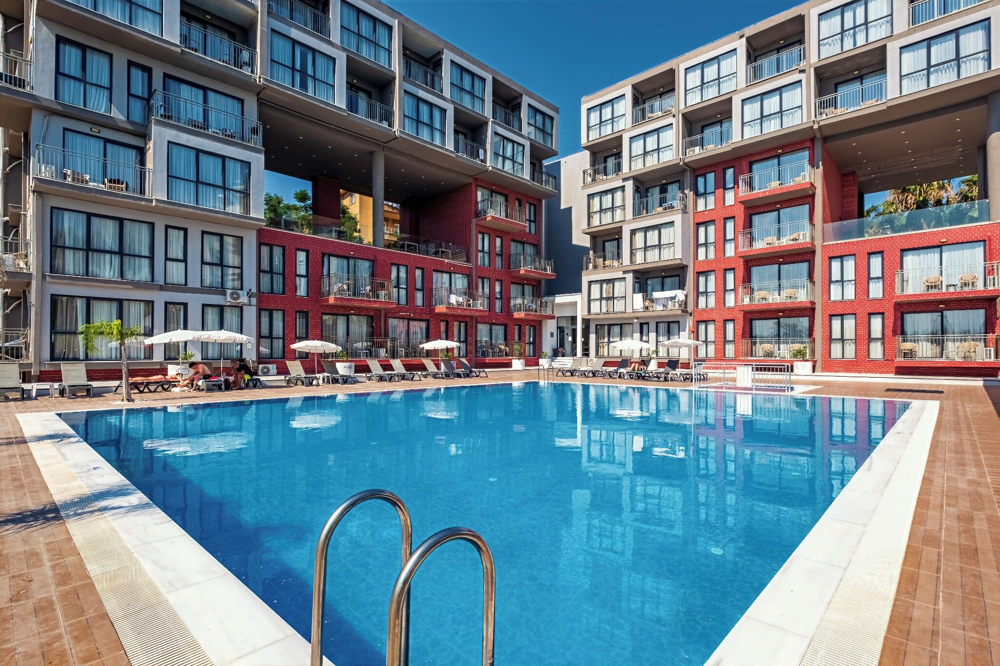 A hotel pool area with multiple levels of balconies, sun loungers, and a clear blue pool.