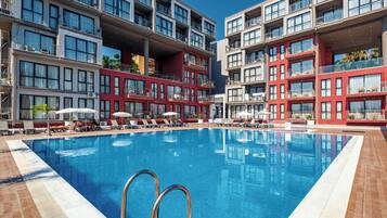 A hotel pool area with multiple levels of balconies, sun loungers, and a clear blue pool.