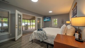 Habitación de hotel con cama, mesita de noche, lámpara, televisor y vista al exterior.