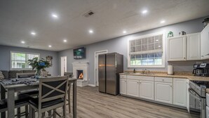 Una cocina moderna con armarios blancos, un refrigerador de acero inoxidable y un comedor con una mesa y sillas de madera.