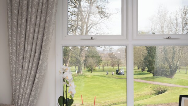 A window with a view of a golf course, a potted orchid, and a decorative bowl on a windowsill. - Shirley's House (Omagh)