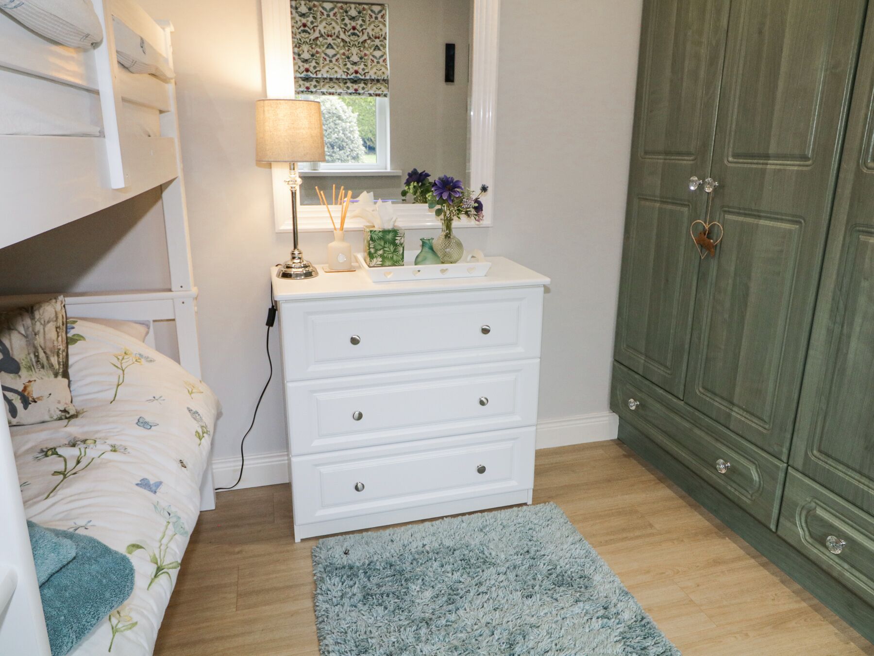 A bedroom with a bed, a dresser, a mirror, a lamp, and a green wardrobe.