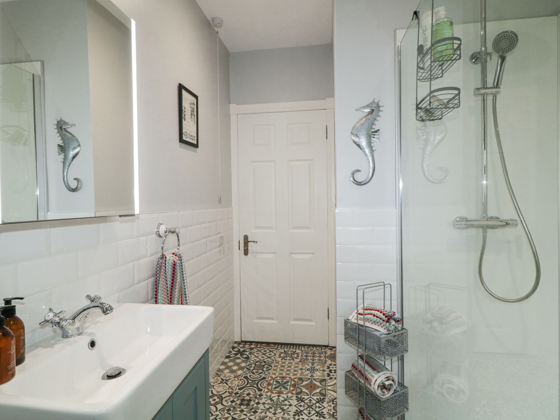 A bathroom with a white sink, a mirror, a door, and a shower with a glass door.