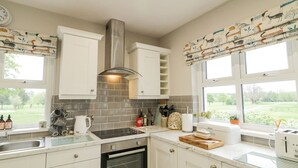 A modern kitchen with white cabinets, a stainless steel range hood, a built-in oven, and a window with a view of the outdoors. - Shirley's House (Omagh)