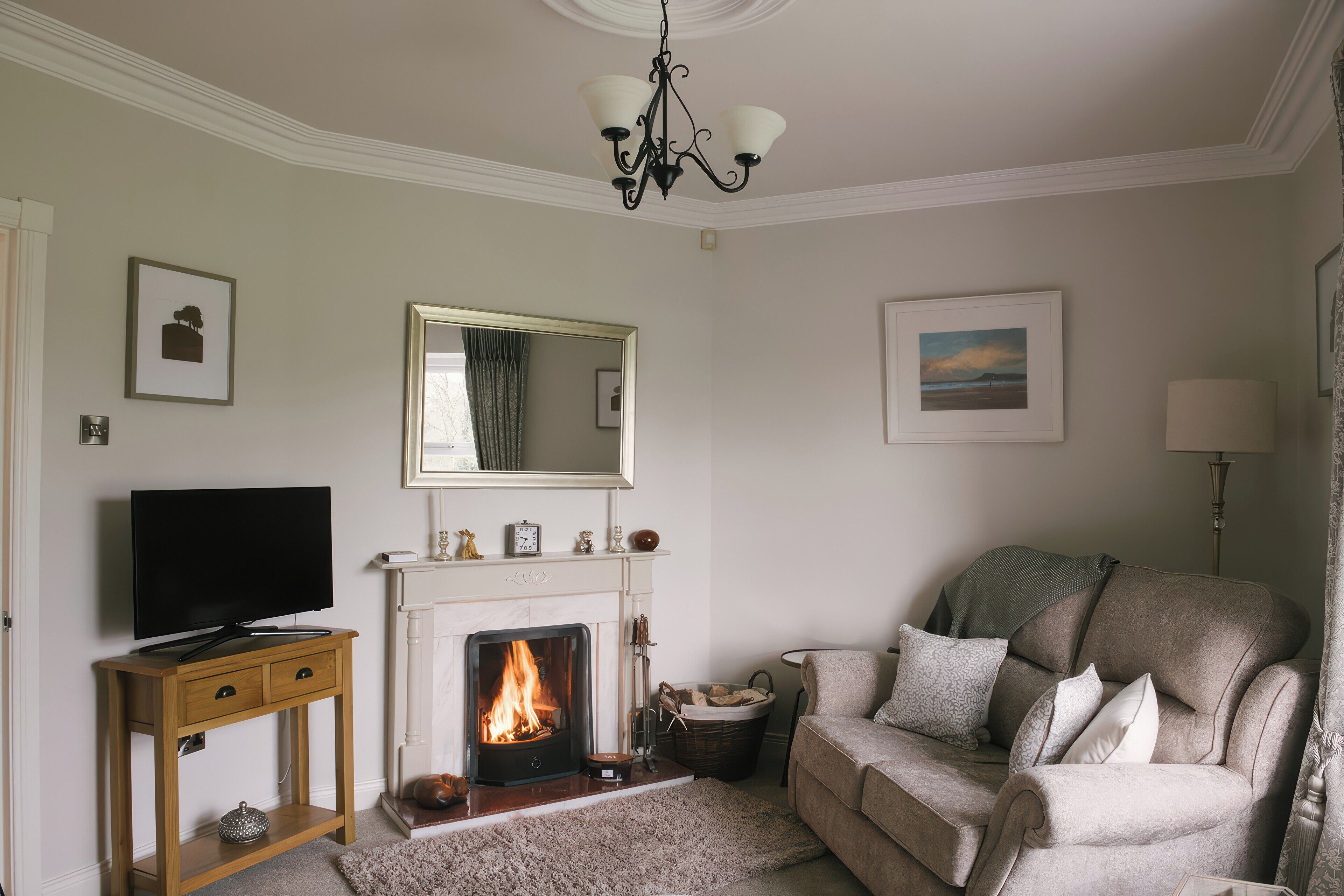 Una sala de estar con chimenea, un televisor sobre un soporte de madera, un sofá y una araña.