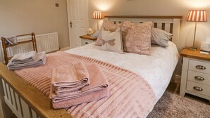 A neatly made bed with a pink blanket and pillows, a wooden headboard, a bedside lamp, and a framed picture on the wall. - Shirley's House (Omagh)