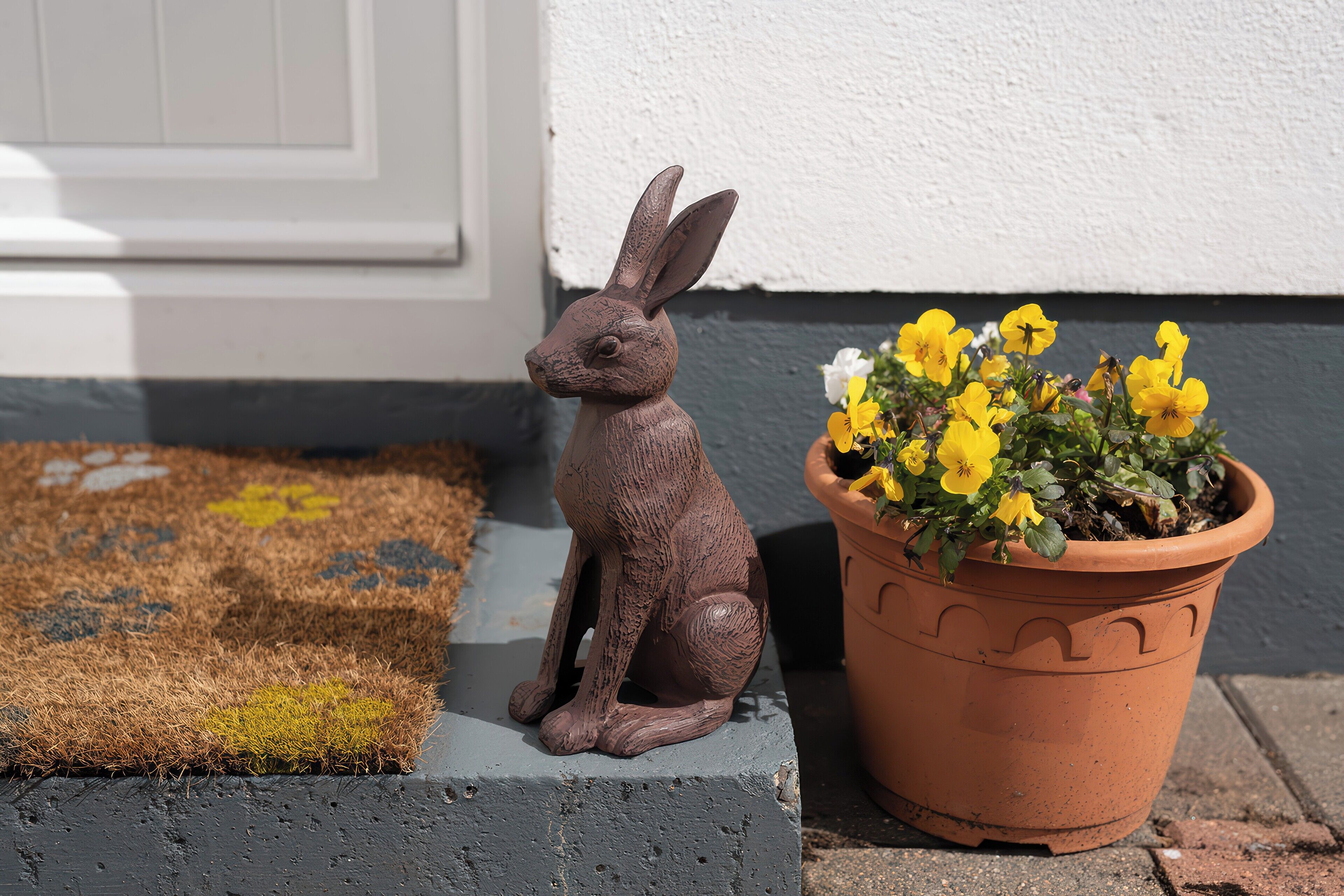 Uma estatueta de coelho ao lado de um vaso de terracota com flores amarelas.