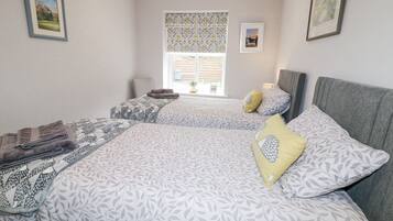 Un dormitorio con dos camas, una ventana con cortinas estampadas y vistas a un edificio.