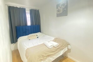 Quarto com cama, cortinas, cabeceira, obra de arte na parede e janela.