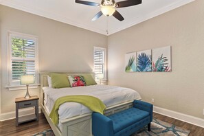 A bedroom with a bed, a nightstand, a blue bench, a ceiling fan, and artwork on the wall. - Mediterranean Home with Club Amenities & Golf Cart (Destin)