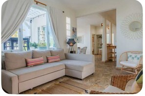 Ein Wohnzimmer mit einem beigefarbenen Ecksofa, einem Korbstuhl und einer Stehlampe.