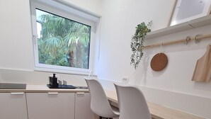 A modern kitchen with white cabinets, two white chairs, a wooden countertop, and a window with a view of greenery.