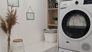 A laundry room with a stacked washer and dryer, a white countertop, a shelf with a potted plant, and two glass jars.
