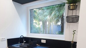 A modern kitchen with a built-in stove, a sink, and a window overlooking a garden. - Balance Deluxe Studio Koper (Koper)