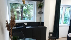 A modern kitchen with a black countertop, a dining table with two chairs, and a hanging pendant light. - Balance Deluxe Studio Koper (Koper)