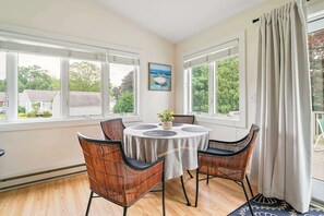 A dining area with a round table, four wicker chairs, a potted plant, and a painting on the wall. - Summer Escape (Wells)