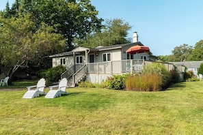 Ein zweistöckiges Haus mit Veranda, Treppe und einem kleinen Gartenbereich mit Stühlen.
