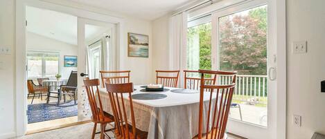 A dining area with a table and chairs, a painting on the wall, and a view through a glass door.