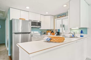 A modern kitchen with white cabinets, stainless steel appliances, and a central island with a woven basket. - Summer Escape (Wells)